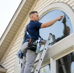 Professional window cleaner on a ladder using a squeegee to clean an exterior arched window, Hialeah, FL.